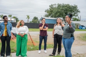 Community members and funders gather outdoors during a site visit, listening as a community leader shares insights about the local neighbourhood
